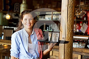 Smiling woman holding tray of drinks at a bar