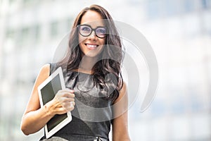 Smiling woman holds a tablet smiling, walking in business clothes outside the office building