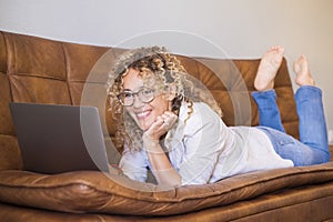 Smiling woman at home watching laptop screen. Portrait of cheerful female adult people using laptop computer comfortably laying on