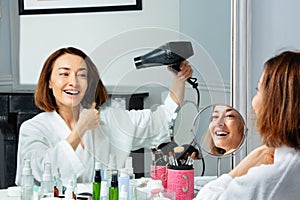 Smiling woman in housecoat holding hairdryer dry hair photo