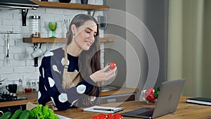 Smiling woman housewife in apron shows teacher chef cherry tomato to webcam