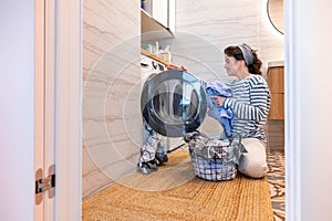 Smiling woman housewife cleaning linen textile clothes putting washing machine and dryer at laundry