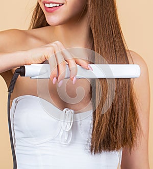Smiling woman ironing long hair with flat iron. Portrait of young beautiful girl using styler on her shining hair