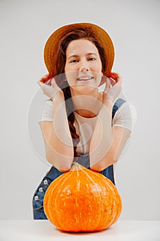 Smiling woman in jumpsuit on a white background with large pumpkin.