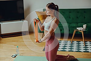 Smiling woman kneeling on yoga mat, holding resistance band for thighs