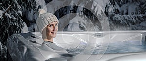 Smiling woman with knitted hat relaxing in outdoor hot tub at snowy winter. banner with copy space