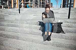Smiling woman with a laptop sitting on the concrete steps
