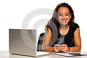 Smiling woman with laptop texting messages on her phone