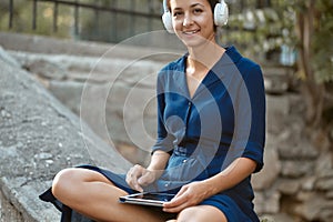 Smiling woman listen music in headset with modern tablet. Relax and joy in park. Leisure time and take break concept