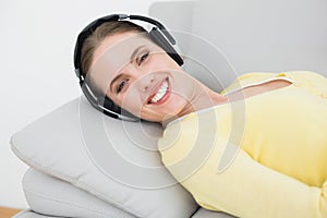 Smiling woman listening music through headphones on sofa