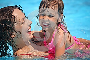 Smiling woman and little girl bathes in pool