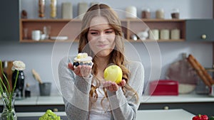 Smiling woman looking at cake and apple in kitchen. Girl preferring fresh fruit. photo