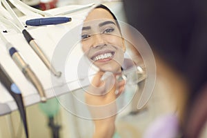 Smiling woman looking at mirror at her teeth after dentist visit