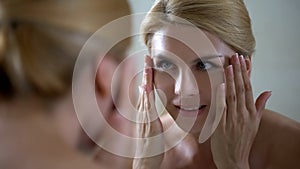 Smiling woman looking in mirror, perfect beautiful skin, rejuvenating injections