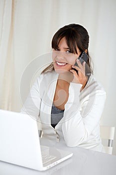 Smiling woman looking at you and using her laptop