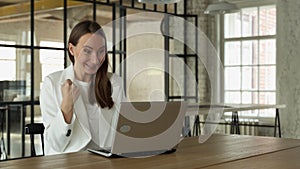 Smiling woman looks at the laptop screen. An excited business woman raises her hands up, has received a good business
