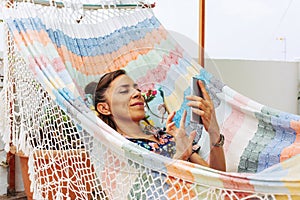 Smiling woman lying in colorful hammock using mobile phone. summer lifestyle