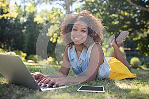 Smiling woman lying on grass and using laptop