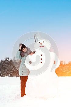 smiling woman makes a snowman on a winter day in a snow-covered field under the open sky.