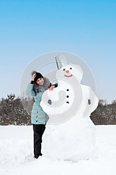 smiling woman makes a snowman on a winter day in a snow-covered field