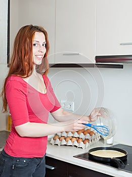 Smiling woman making scrambled eggs in frying pan