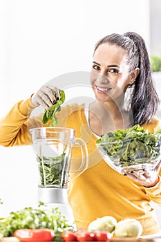 Smiling woman making spinach smoothie, putting leaves in blender
