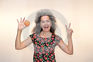 Smiling woman making V sign and holding orange