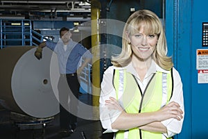 Smiling Woman With Man By Huge Roll Of Paper In Factory