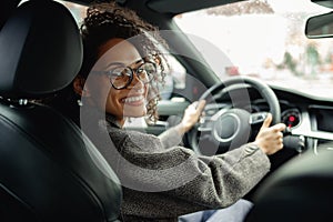 Smiling woman manager driving car and holding both hands on steering wheel on the way to work