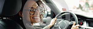 Smiling woman manager driving car and holding both hands on steering wheel on the way to work