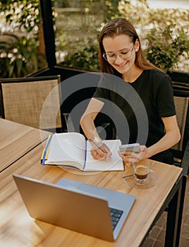 Smiling woman manager use phone and work on laptop in cafe terrace. Distance work concept