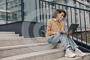 Smiling woman manager working laptop sitting on stairs on modern building background