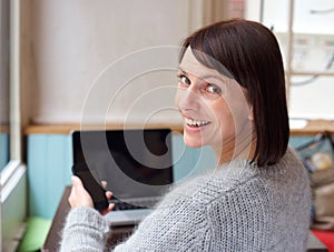 Smiling woman with mobile phone and laptop at home