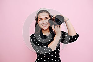 Smiling woman in modest clothes posing with her digital camera over pink