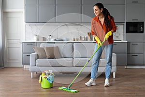 Smiling woman mopping floor with a bucket of supplies nearby