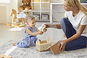 Smiling woman mother sitting with her small baby boy on floor, giving him wooden toy and playing together