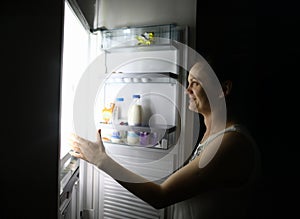 Smiling woman at night at home opened refrigerator