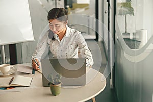 Smiling woman office manager making notes while working on laptop in modern coworking