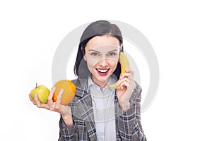 smiling woman in office suit holding an apple and an orange in one hand, calling a banana with the other hand, healthy