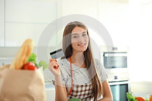 Smiling woman online shopping using computer and credit card in kitchen.