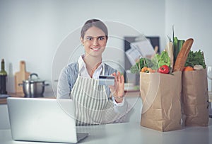 Smiling woman online shopping using computer and credit card in kitchen