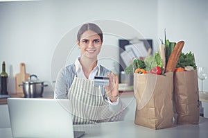 Smiling woman online shopping using computer and credit card in kitchen