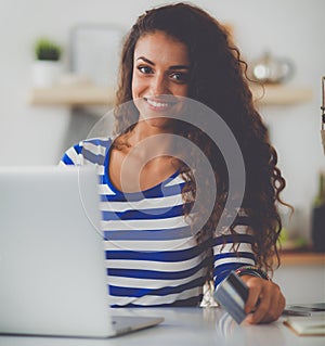 Smiling woman online shopping using computer and credit card in kitchen