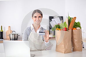 Smiling woman online shopping using computer and credit card in kitchen