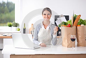 Smiling woman online shopping using computer and credit card in kitchen