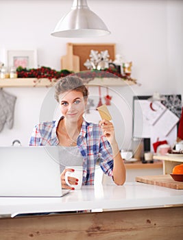 Smiling woman online shopping using computer and credit card in kitchen