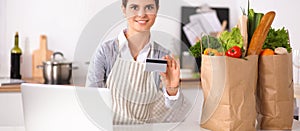 Smiling woman online shopping using computer and credit card in kitchen