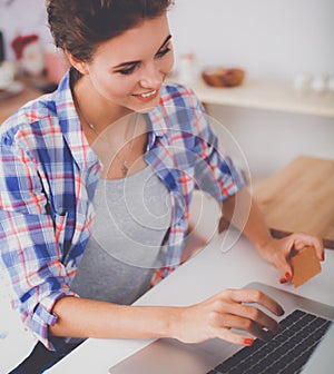 Smiling woman online shopping using computer and credit card in kitchen