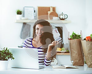 Smiling woman online shopping using computer and credit card in kitchen