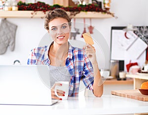 Smiling woman online shopping using computer and credit card in kitchen